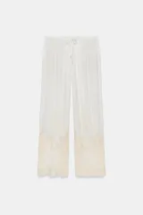 Pantalón de tiro medio con cintura elástica ajustable mediante cordones. Presenta un diseño fluido con bolsillos laterales ocultos y bajo decorado con una aplicación de encaje a contraste.