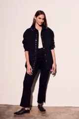 Sobrecamisa negra de algodón con corte oversize, cuello clásico, cierre frontal con botones a presión, dos bolsillos de parche en el pecho y apliques metálicos en cuello y solapa.