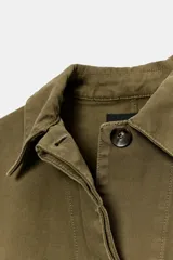 Chaqueta de estilo utilitario color verde militar, con cuello solapa, manga larga y cierre frontal con botones ocultos por solapa. Presenta bolsillos con solapa en la parte delantera y un bolsillo de plastrón en el pecho.