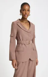 Blazer sastre color marrón claro con patrón de raya diplomática, cuello con solapa ancha, mangas largas con bolsillos aplicados en las mangas, bolsillos frontales con solapa, cinturón incorporado con hebilla metálica y cierre cruzado.