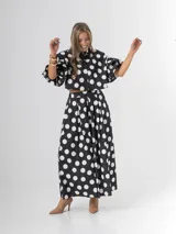 Conjunto de dos piezas con estampa polka dots en negro y blanco, compuesto por un pantalón tipo culotte de tiro alto con bolsillos y una blusa estilo camisa con mangas globo y cierre frontal de botones.