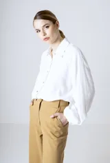 Camisa blanca de manga larga holgada, con cuello camisero, cierre frontal de botones y puños fruncidos con elástico.