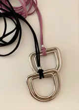 Collar de cordón de gamuza sintética con dije metálico de diseño geométrico o circular. El diseño permite diversas formas de uso, ya sea atado al cuello o con el dije al frente.