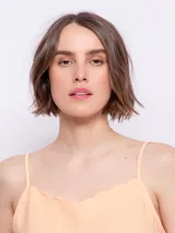 Top color durazno de breteles finos y escote con terminación ondulada.