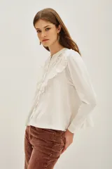 Camisa de manga larga color negro, con cuello redondo y cierre frontal de botones. Presenta un diseño con volados en la parte superior delantera y detalles de encaje bordado en los hombros y pecho.