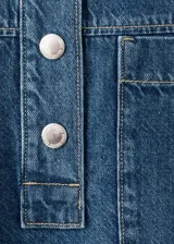Blusa de algodón estilo denim, con diseño oversize, cuello camisero, mangas cortas, dos bolsillos de parche en el pecho y cierre frontal de botones.