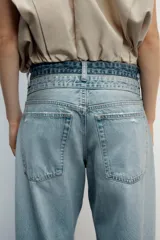 Jeans de tiro medio con cinco bolsillos, diseño holgado y efecto desgastado con detalles de rotos. Cuenta con una cintura doble combinada en contraste de tonos denim y cierre frontal con cremallera y botones metálicos.