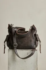 Cartera mini de cuero marrón con terminación gastada, cuerpo blando, bolsillos exteriores y solapa con cierre de hebilla. Incluye herrajes metálicos envejecidos y detalles colgantes con candado y llave.