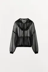 Cazadora de tejido de red semitransparente color negro, con capucha, cierre frontal de cremallera metálica, bolsillos delanteros y mangas largas con puños elásticos.