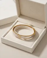 Pulsera tipo esclava rígida de acero inoxidable con baño de oro, que presenta un diseño bicolor con secciones lisas y una sección central texturizada.