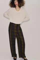 Pantalón de tiro alto con diseño fluido y estampado de cuadros en tonos oscuros. Presenta pliegues frontales, bolsillos delanteros con solapa y cierre frontal con cremallera, botón y ganchos metálicos.