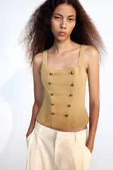 Top corsetero de color tostado con escote cuadrado, tirantes anchos y cierre de cremallera en la espalda. Cuenta con costuras marcadas y filas de botones metálicos dorados decorativos en el frente.