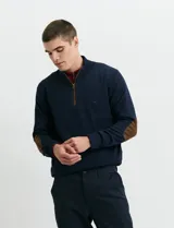 Sweater de punto color verde oliva, con cuello alto y medio cierre frontal. Presenta coderas en símil nappa y puños acanalados.