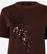 Remera de algodón de corte recto, con cuello redondo y mangas cortas. Presenta un diseño decorativo de lentejuelas bordadas en la parte frontal.