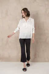 Blusa blanca de manga larga con cuello camisero y cierre frontal parcial con botones.