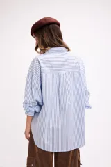 Camisa de corte oversize con estampado de rayas verticales finas en color marrón sobre fondo blanco. Presenta cuello clásico, cierre frontal con botones, bolsillo en el pecho y mangas largas con puños abotonados.