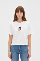 Remera cropped de algodón blanca, de corte holgado, con cuello a la base, manga corta y estampa centrada en el pecho con diseño ilustrado.