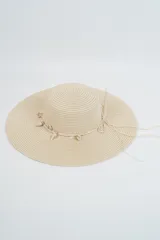 Sombrero de paja tejido color beige, de ala ancha y copa redonda, decorado con una sarta de caracoles marinos colgantes.