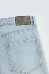 Bermudas de denim de algodón, color celeste claro con efecto lavado y manchas marrones/beige en las perneras. Tienen un corte ancho (baggy fit) y terminación de bajo irregular.