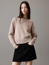 Sweater color beige de punto de algodón orgánico, con cuello redondo alto, mangas largas y logo bordado en el pecho.