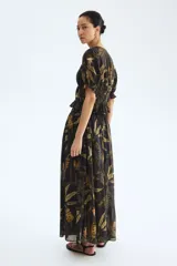 Pollera larga de corte holgado, color negro, con estampado tropical de hojas y flores en tonos verdes y ocres. Presenta tiro alto, cintura elastizada en la espalda con frunces y diseño fluido.