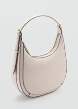 Bolso de hombro tipo hobo en color beige, con diseño de media luna, cierre de cremallera y asa ajustable con hebillas laterales.