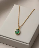 Collar de cadena fina dorada con dije ovalado de piedra verde esmeralda en marco de bronce.