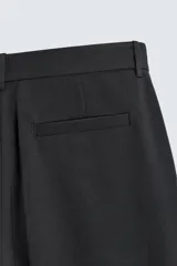 Pantalón de corte relaxed fit confeccionado en tejido con mezcla de lana, con bolsillos delanteros y traseros de vivo, cierre frontal con cremallera y botón.
