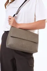 Bandolera de cuero sintético negro con solapa frontal y herrajes plateados. Incluye una correa ajustable y extraíble con diseño de rayas en tonos beige y negro.