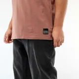 Remera de manga corta marrón, de corte holgado y escote en V, con pequeña etiqueta decorativa en el dobladillo inferior.
