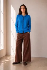 Cardigan de punto azul con ribetes en contraste negro, cuello redondo, cierre frontal con botones y bordado pequeño en el pecho.