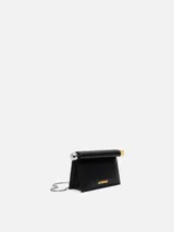 Bolso de cuero color negro modelo La Petite Pochette Rond C de Jacquemus, con silueta de sobre, solapa superior enrollada con broche magnético, extremos metálicos en plata y oro, y logo grabado en letras doradas en el frente.