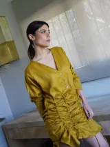 Vestido corto de lino mostaza con escote en V, mangas largas y fruncidos laterales regulables mediante cordones.