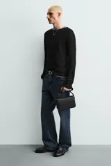 Bandolera negra con textura grabada, compartimento principal con cierre de solapa imantada, bolsillo interior con cremallera y asa de hombro ajustable.