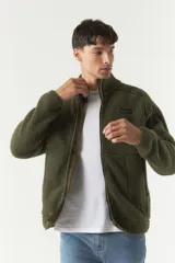 Campera de sherpa color verde militar, con cierre frontal completo, cuello alto y bolsillos laterales con cierre. Presenta un parche pequeño con logo en el pecho.