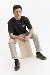 Remera de manga corta color negro con cuello redondo y un estampado frontal en tonos morados y blancos que incluye texto y un diseño floral.