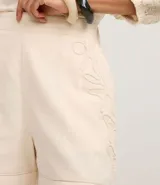 Short de cintura alta color crema, con bolsillos laterales y bordados abstractos en los costados.