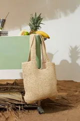 Cartera tipo canasto playero de color beige, confeccionada en papiro con diseño tejido a crochet, asas de hombro y cierre en el compartimento principal.