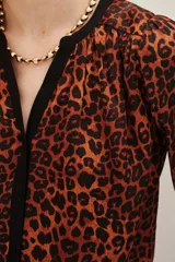 Camisa de manga larga con estampado animal print en tonos caramelo y negro. Presenta un escote en V con una solapa central en color negro y puños elásticos.