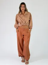 Pantalón de lino color beige, de corte holgado tipo jogger con puños ajustables con cintas en los tobillos, bolsillos laterales y cierre frontal con botón y cremallera.
