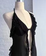 Top halter negro de microtul transparente, con escote en V profundo y bordes con volados o festones. Presenta un cierre frontal central.