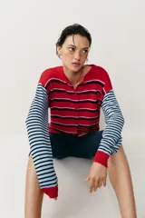 Chaqueta de punto con cuello redondo y mangas largas, con diseño de rayas horizontales en colores rojo, celeste y azul marino, y cierre frontal con botones.