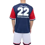 Remera de fútbol Umbro del Club Nacional de Football, modelo Match en color azul marino con mangas y canesú rojos. Cuenta con cuello en V con detalles blancos y azules, y el escudo del club bordado en el pecho.