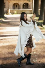 Ruana de lana merino color crudo, con diseño de silueta amplia y caída fluida. Presenta detalles de volados en lino a lo largo de la prenda y terminaciones con flecos en el ruedo.