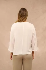 Blusa color crudo de mangas 3/4, escote en V con abotonadura frontal y sutiles pliegues en la parte delantera.