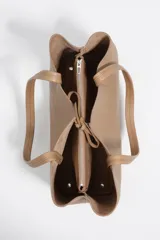 Bolso shopper de piel color borgoña, con textura granulada, asas de hombro y cierre de cordón. Presenta el logo metálico de Bimba y Lola en el frente.