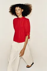 Blusa blanca de cuello alto con detalles de puntilla, manga corta abullonada y cierre posterior con botón.