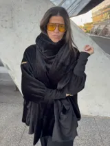 Bata de diseño holgado confeccionada en tela de textura suave y aterciopelada, color negro. Presenta una capucha amplia que puede utilizarse como bufanda, puños elásticos ajustados y bolsillos laterales.