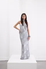 Vestido largo plateado con acabado metalizado, escote halter con cuello cruzado regulable, espalda descubierta y tajo trasero.