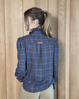 Camisa de manga larga con estampado de cuadros en tonos marrones y azules. Presenta cuello alto con volados, cierre frontal con botones y puños con volados.